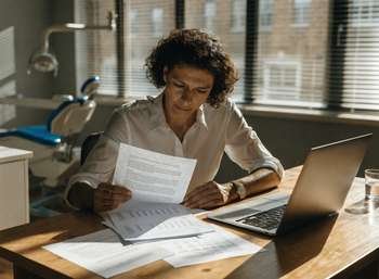 Dental practice owner reviewing a letter and financial figures at a desk