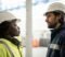Two employees in work clothing talking on site during a business transfer